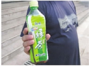 周先生拿着内含黄色不明沉淀物的半瓶康师傅绿茶。 周先生拿着内含黄色不明沉淀物的半瓶康师傅绿茶。
